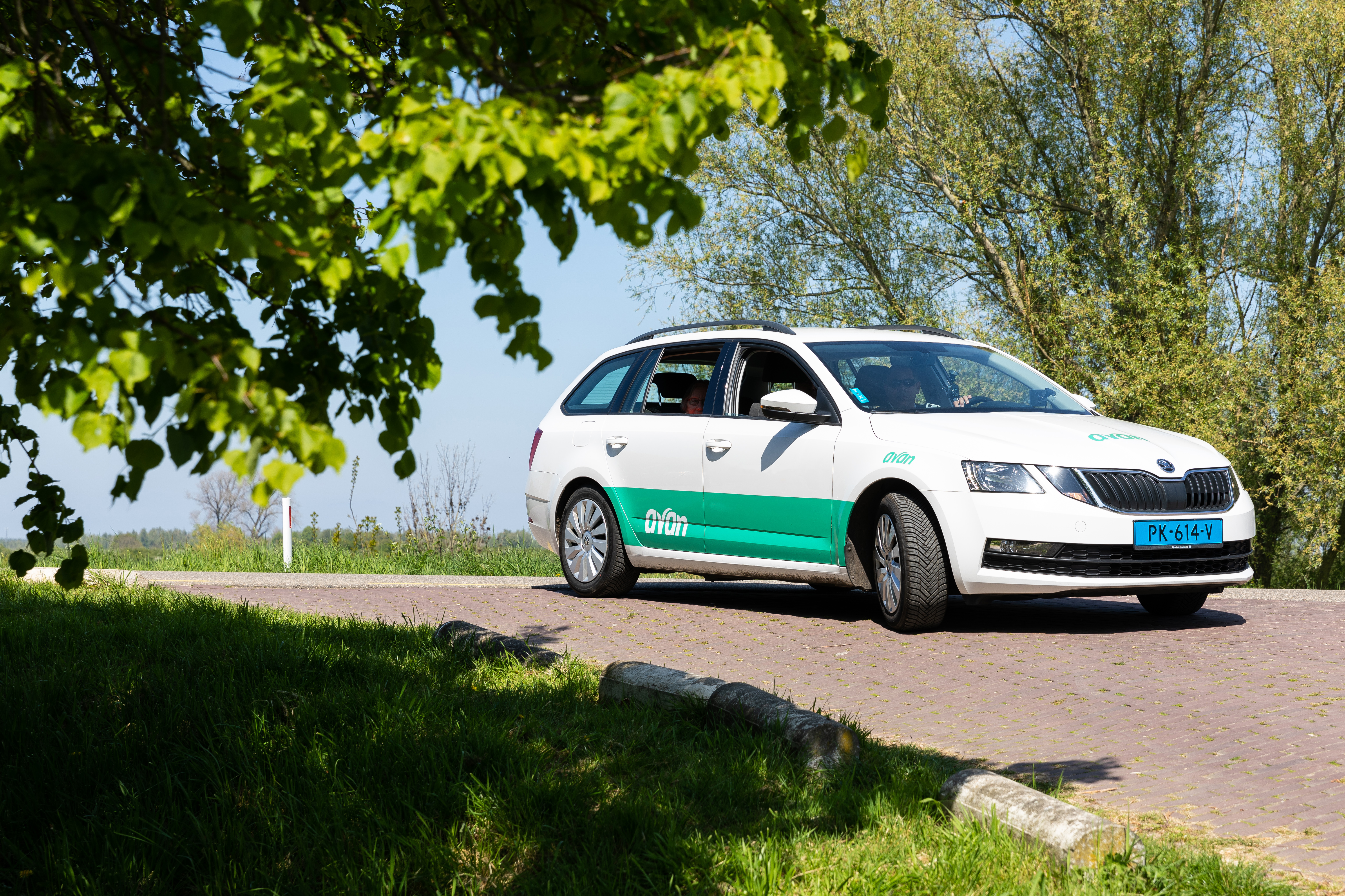 Een personenauto van Avan rijdt over de dijk op een zonnige dag.